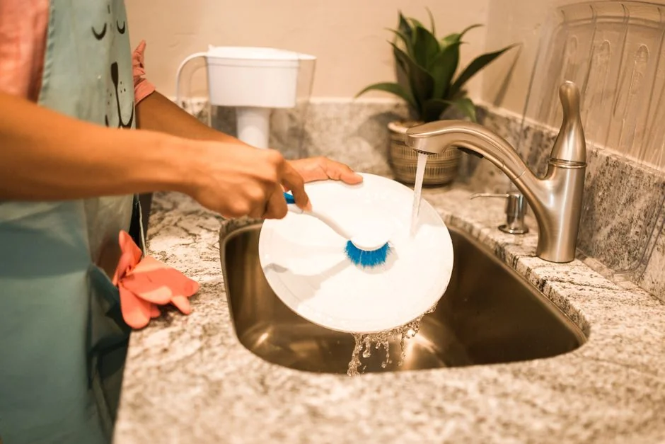 A hand wipes a dark surface with a tissue near a paper roll and plant.